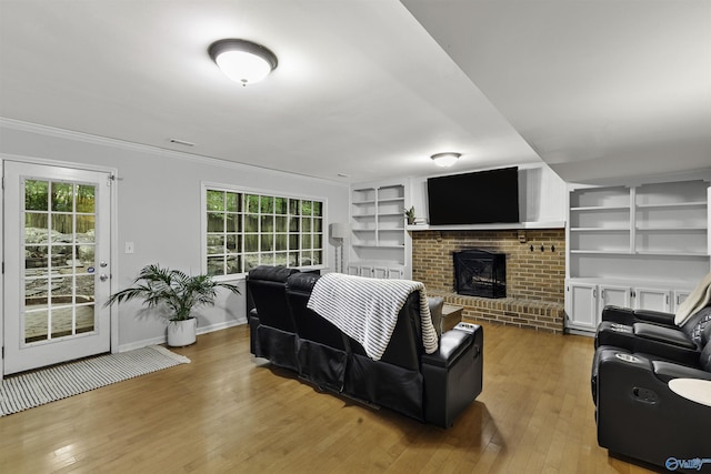 living area with a wealth of natural light, a brick fireplace, hardwood / wood-style flooring, and built in features