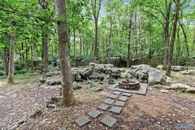 view of yard featuring fence, a fire pit, and a view of trees