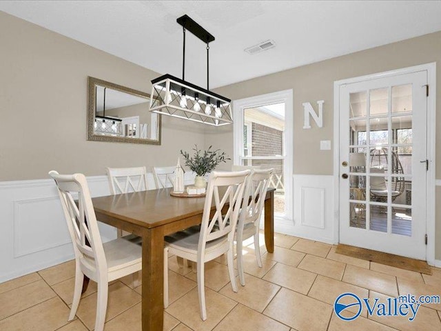 dining room featuring visible vents, light tile patterned flooring, and wainscoting