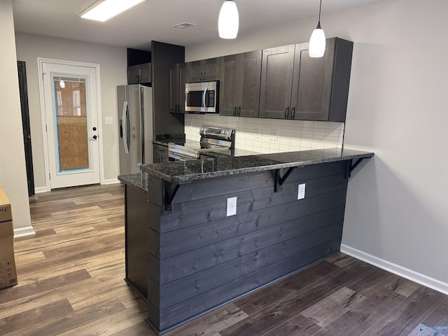 kitchen with decorative backsplash, wood finished floors, stainless steel appliances, dark stone countertops, and a kitchen breakfast bar