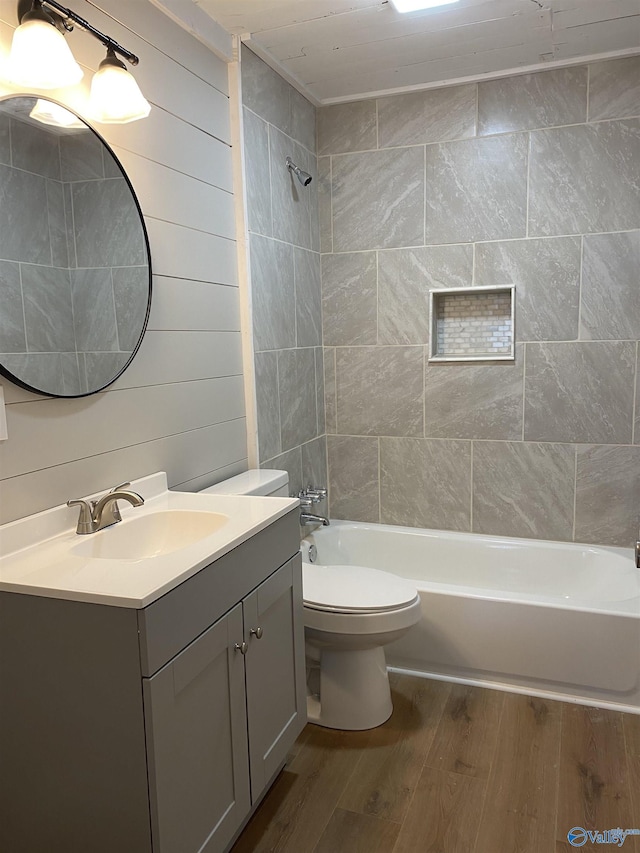 full bathroom with toilet, wood walls, tiled shower / bath, vanity, and hardwood / wood-style flooring