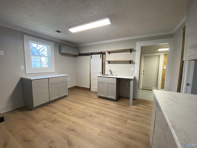 kitchen with sink, gray cabinets, a textured ceiling, a barn door, and light wood-type flooring