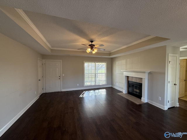 unfurnished living room featuring a raised ceiling, dark wood-type flooring, a tiled fireplace, a textured ceiling, and baseboards