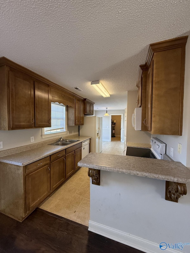 kitchen with light countertops, a peninsula, white appliances, a textured ceiling, and a sink