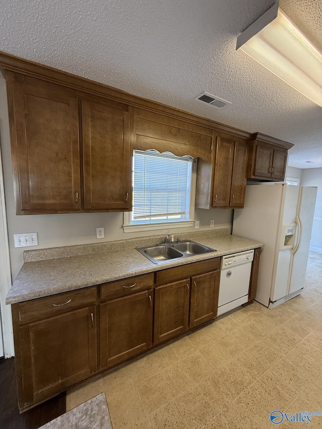 kitchen featuring visible vents, light floors, white appliances, a textured ceiling, and a sink