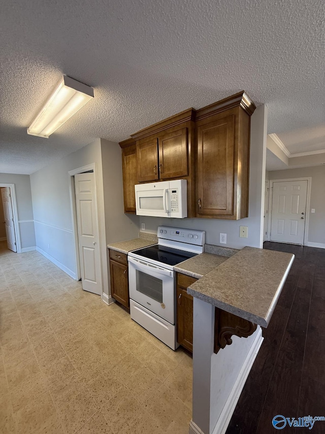 kitchen with dark countertops, baseboards, a peninsula, white appliances, and a textured ceiling