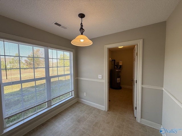 unfurnished dining area featuring water heater, visible vents, a textured ceiling, and baseboards