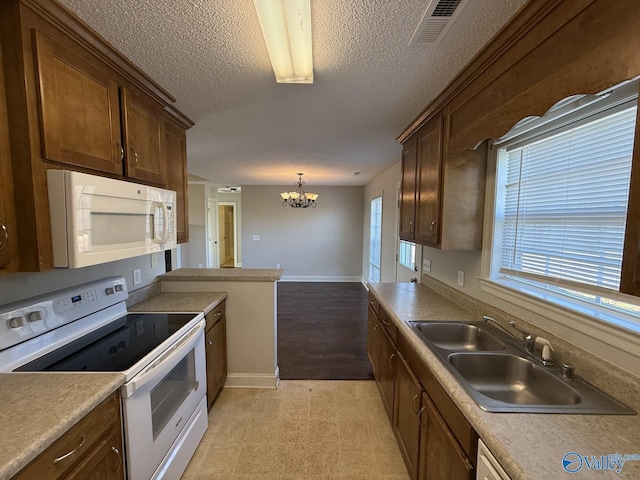 kitchen with visible vents, a chandelier, white appliances, a textured ceiling, and a sink