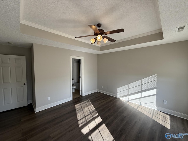 empty room with a tray ceiling, baseboards, dark wood-type flooring, and visible vents