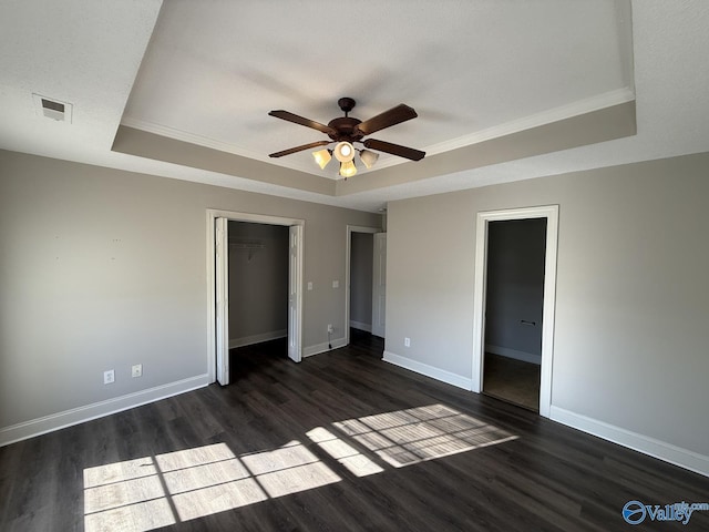 unfurnished bedroom with dark wood-style floors, visible vents, baseboards, and a tray ceiling