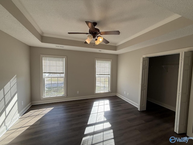 unfurnished bedroom featuring dark wood finished floors, multiple windows, and a tray ceiling