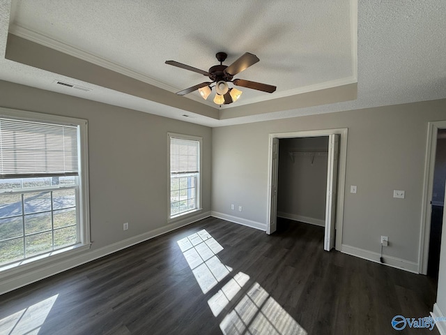 unfurnished bedroom featuring visible vents, a raised ceiling, multiple windows, and dark wood-style flooring