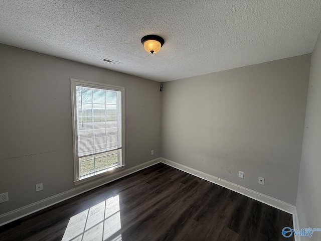 spare room featuring visible vents, a textured ceiling, dark wood-type flooring, and baseboards