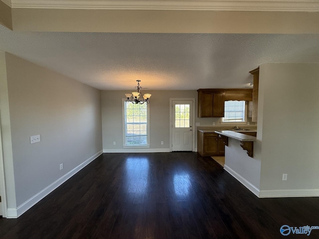 kitchen with a sink, a textured ceiling, dark wood-style floors, an inviting chandelier, and baseboards