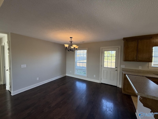 kitchen featuring dark wood-type flooring, decorative light fixtures, a textured ceiling, baseboards, and a chandelier