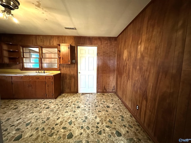 kitchen featuring visible vents, stone floors, brown cabinets, a sink, and wooden walls