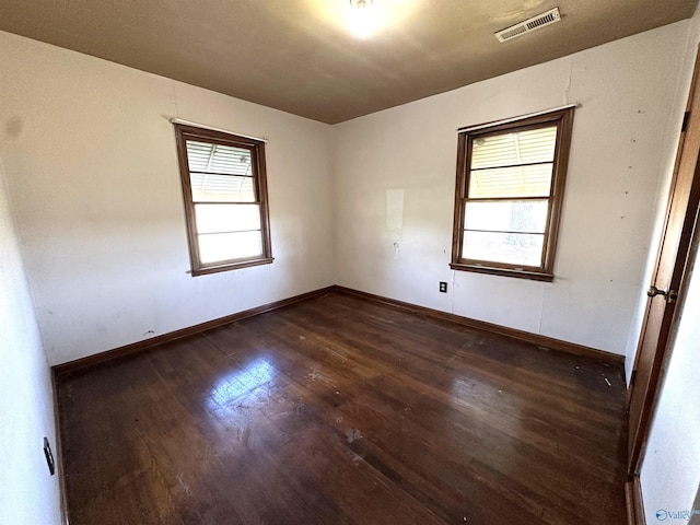 unfurnished room with baseboards, dark wood-type flooring, and visible vents