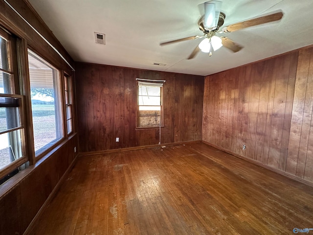 unfurnished room featuring wood walls, wood-type flooring, and ceiling fan