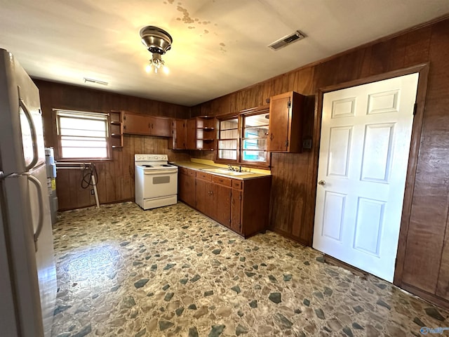 kitchen featuring fridge, white range with electric stovetop, sink, and wooden walls