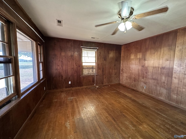 empty room with wood-type flooring, wooden walls, a ceiling fan, and visible vents