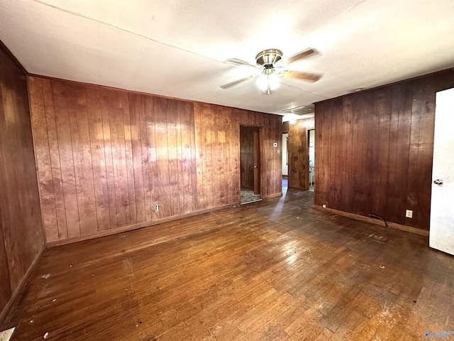 empty room with a ceiling fan, wood walls, and wood finished floors