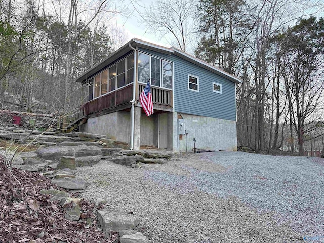 view of home's exterior with gravel driveway, a sunroom, and stairs