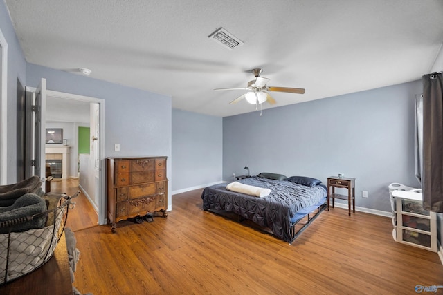 bedroom with hardwood / wood-style flooring, a tiled fireplace, and ceiling fan