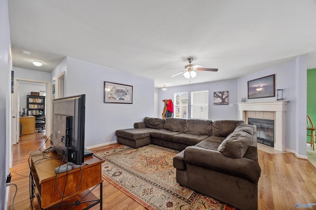 living room with a tiled fireplace, ceiling fan, and light hardwood / wood-style floors