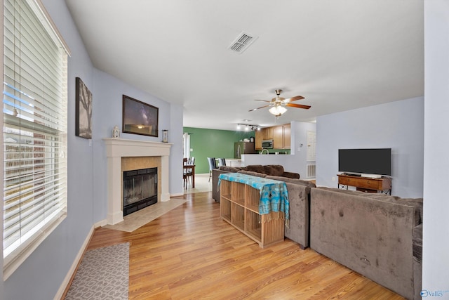 living room with a tile fireplace, plenty of natural light, ceiling fan, and light hardwood / wood-style flooring