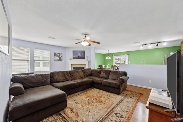 living room featuring hardwood / wood-style flooring, ceiling fan, a tiled fireplace, and a textured ceiling