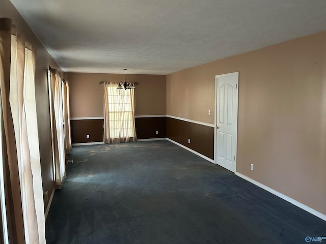 carpeted spare room with a textured ceiling and a notable chandelier