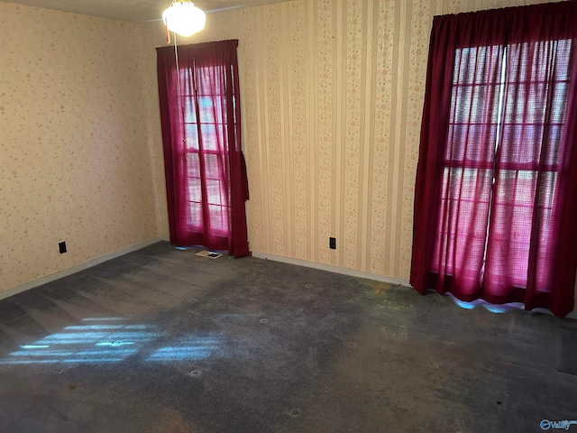 empty room featuring ceiling fan, a healthy amount of sunlight, and dark carpet