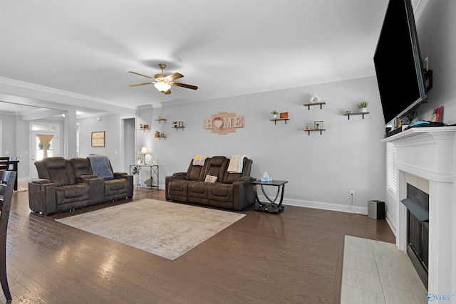 living area with baseboards, a fireplace, a ceiling fan, crown molding, and wood finished floors
