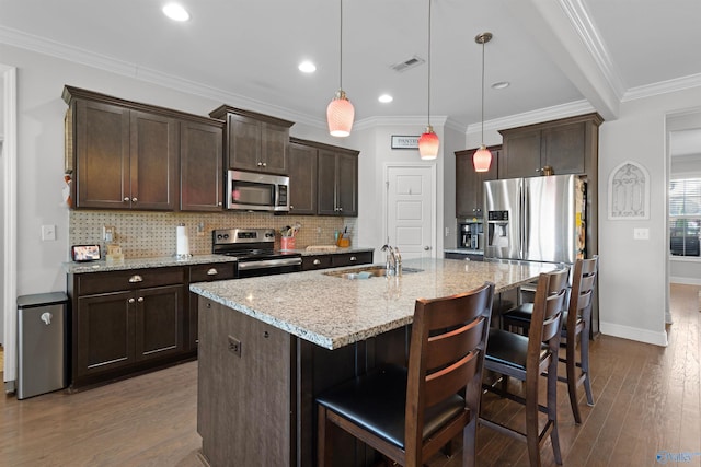 kitchen with appliances with stainless steel finishes, dark brown cabinetry, decorative backsplash, hardwood / wood-style flooring, and a sink