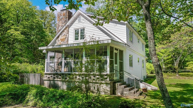 view of property exterior featuring fence, a chimney, a lawn, and a sunroom