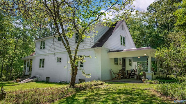 rear view of house with a lawn, a patio, and roof with shingles