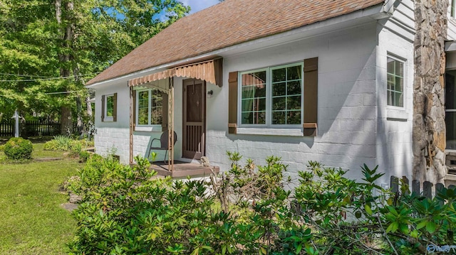 doorway to property featuring fence, a yard, concrete block siding, and roof with shingles