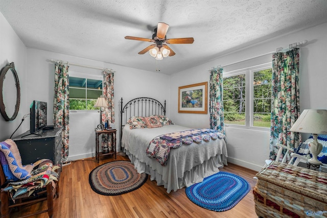 bedroom with a textured ceiling, wood-type flooring, and ceiling fan