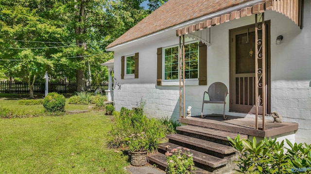 view of side of property featuring a lawn, roof with shingles, concrete block siding, and fence