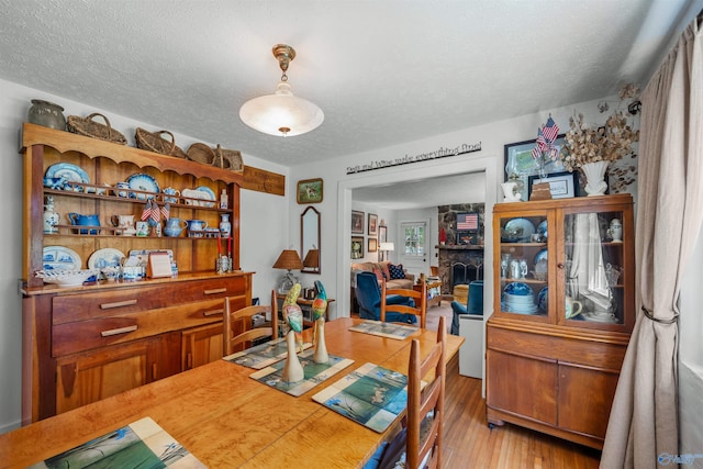 dining room with a fireplace, light wood-type flooring, and a textured ceiling