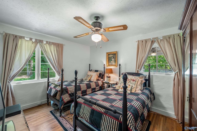 bedroom with a textured ceiling, light hardwood / wood-style flooring, ceiling fan, and multiple windows