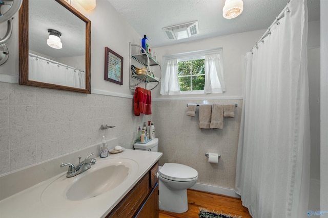 bathroom with toilet, vanity, a textured ceiling, wood-type flooring, and tile walls