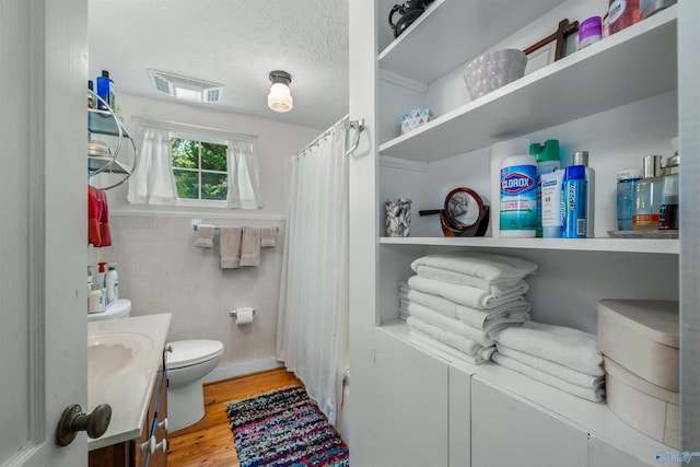 bathroom with a textured ceiling, vanity, walk in shower, toilet, and hardwood / wood-style flooring