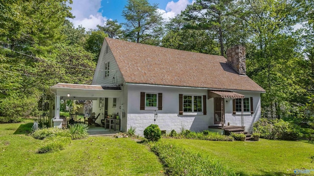view of front of home featuring a shingled roof, a chimney, a front lawn, and concrete block siding