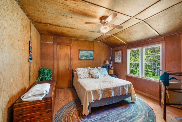 bedroom with lofted ceiling, ceiling fan, wood-type flooring, and wooden walls