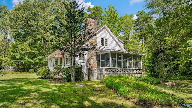 view of property exterior with fence, stone siding, a chimney, a lawn, and a sunroom