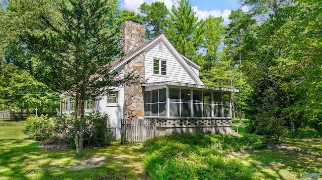 view of home's exterior with stone siding, a chimney, fence, a yard, and a sunroom