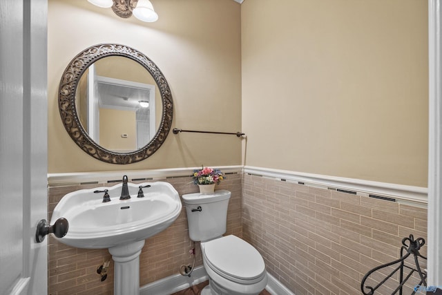 bathroom featuring toilet, tile walls, and wainscoting