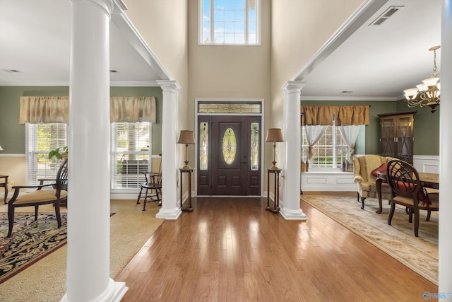 foyer with ornamental molding, hardwood / wood-style flooring, an inviting chandelier, and decorative columns