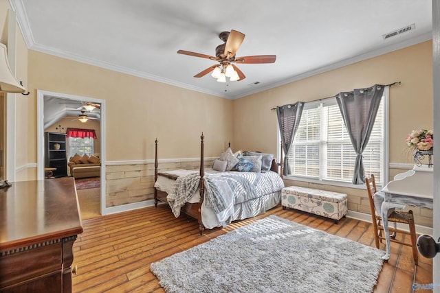 bedroom with visible vents, a ceiling fan, wainscoting, hardwood / wood-style flooring, and ornamental molding